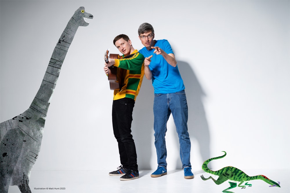 Man with a guitar besides a man pointing at the camera, with an illustrated dinosaur either side